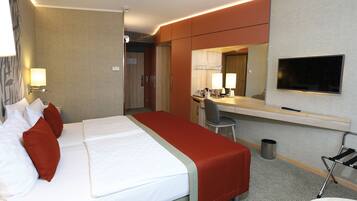 A hotel room with a bed, a desk, a chair, a TV, and a small kitchenette.