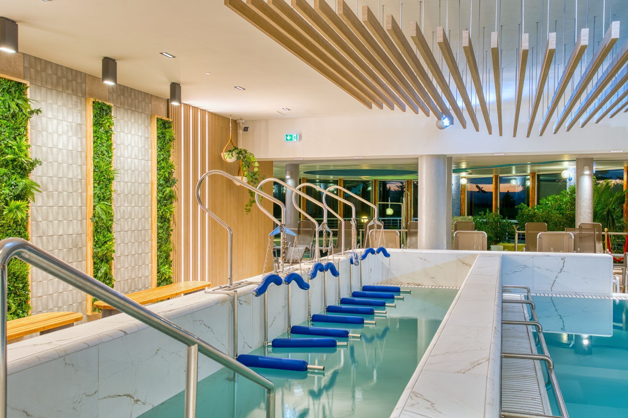 A swimming pool with a marble border, a wooden staircase, and green vertical gardens.