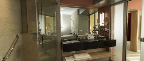 A modern bathroom with a glass shower enclosure, a black countertop sink, and a wooden shelf with towels.