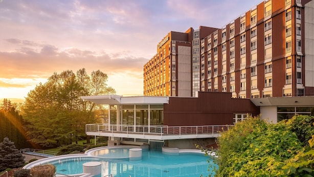A hotel with a swimming pool, a modern building, and a surrounding garden. - Ensana Thermal Aqua (Hévíz)