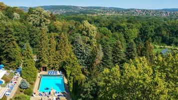 Luchtbeeld van een resort met een zwembad, omgeven door weelderige begroeiing en een in de verte gelegen stad.