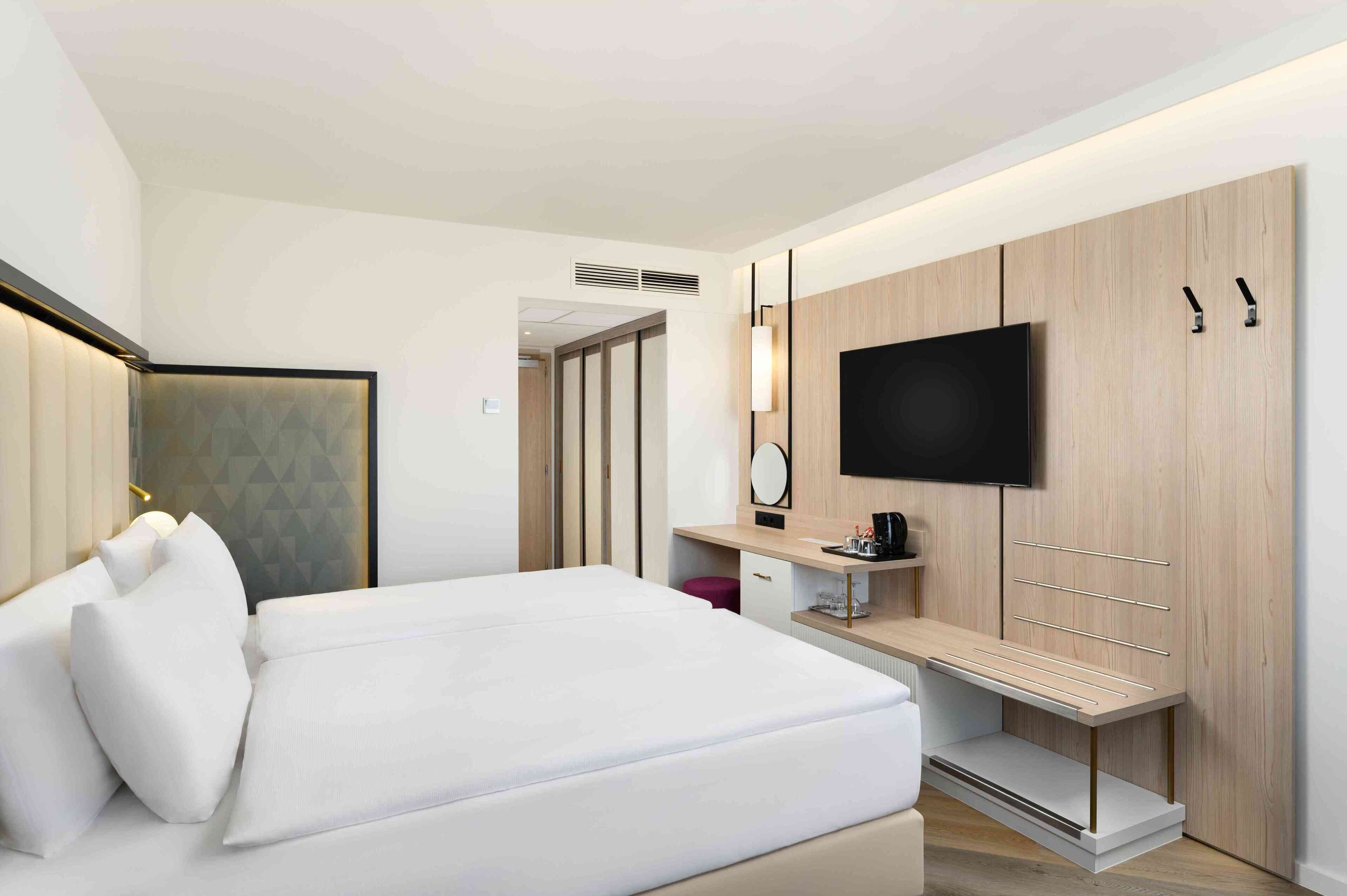 Una habitación de hotel moderna con una cama grande, un televisor montado en una pared de paneles de madera, un escritorio con una silla y un armario.