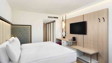 Una habitación de hotel moderna con una cama grande, un televisor montado en una pared de paneles de madera, un escritorio con una silla y un armario.