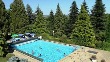 Una piscina rodeada de árboles, con sillas de descanso y sombrillas.