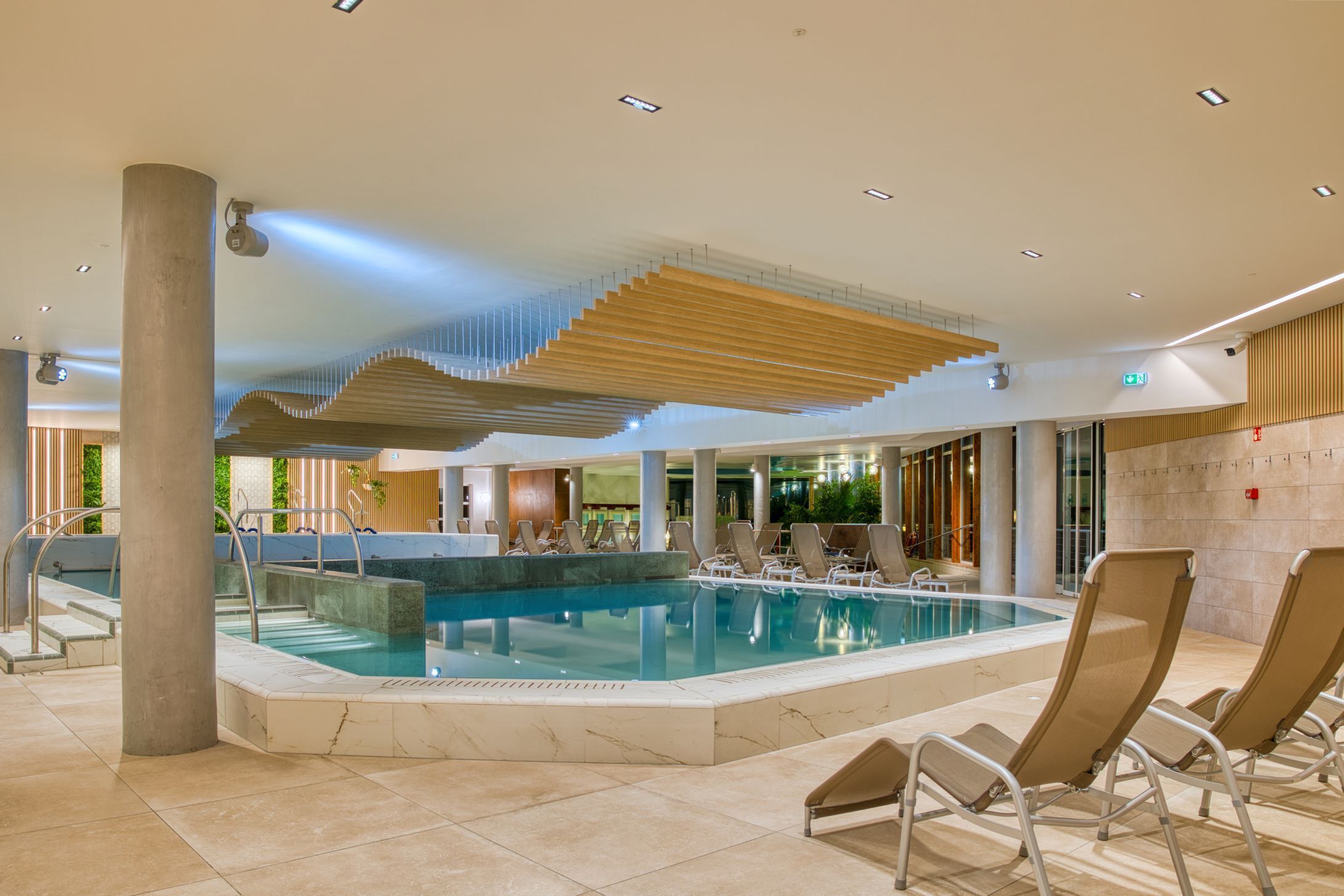 A pool area with lounge chairs, a staircase, and a modern ceiling design.