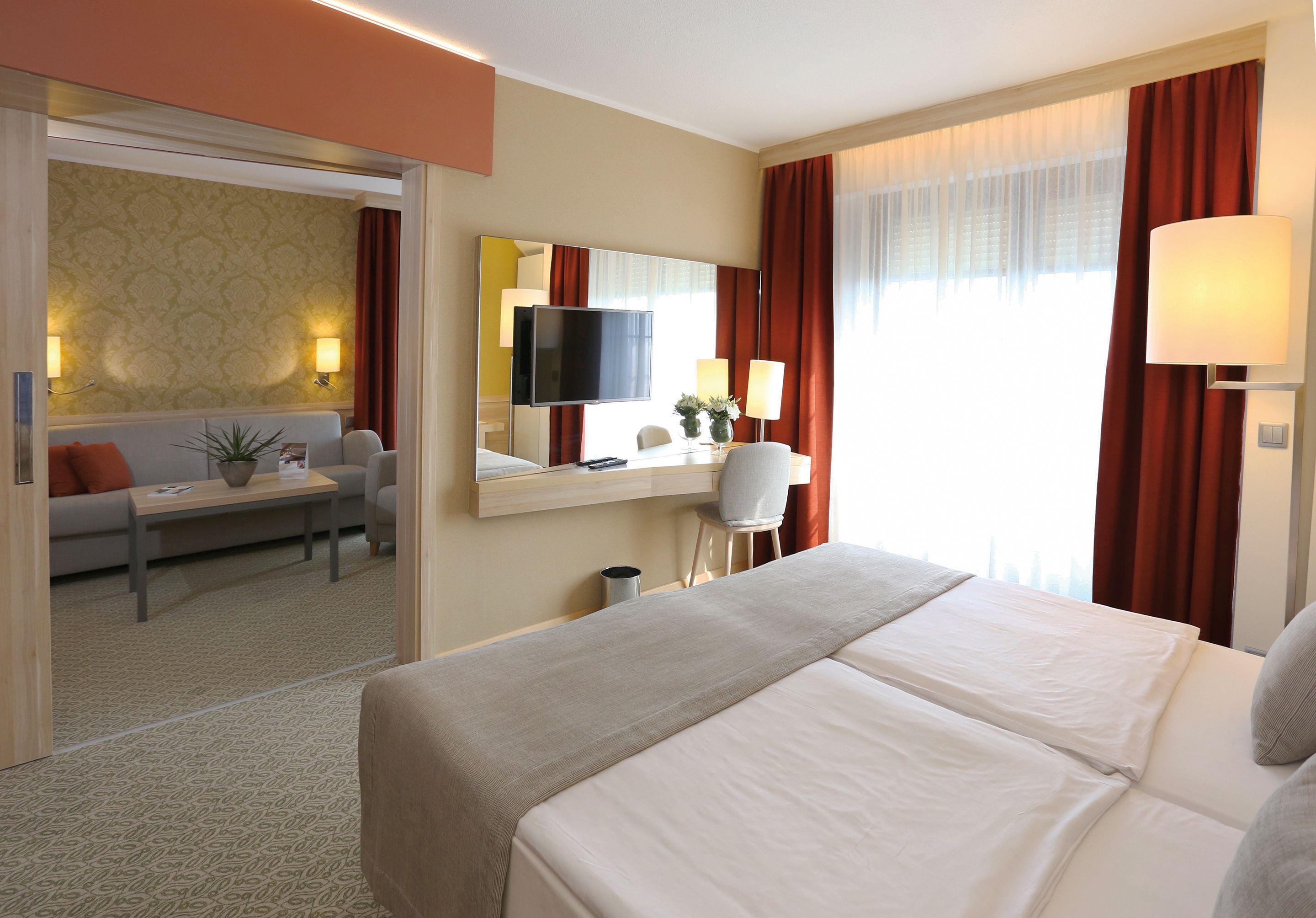 Una habitación de hotel con una cama grande, un escritorio con silla, televisión y ventana con cortinas.