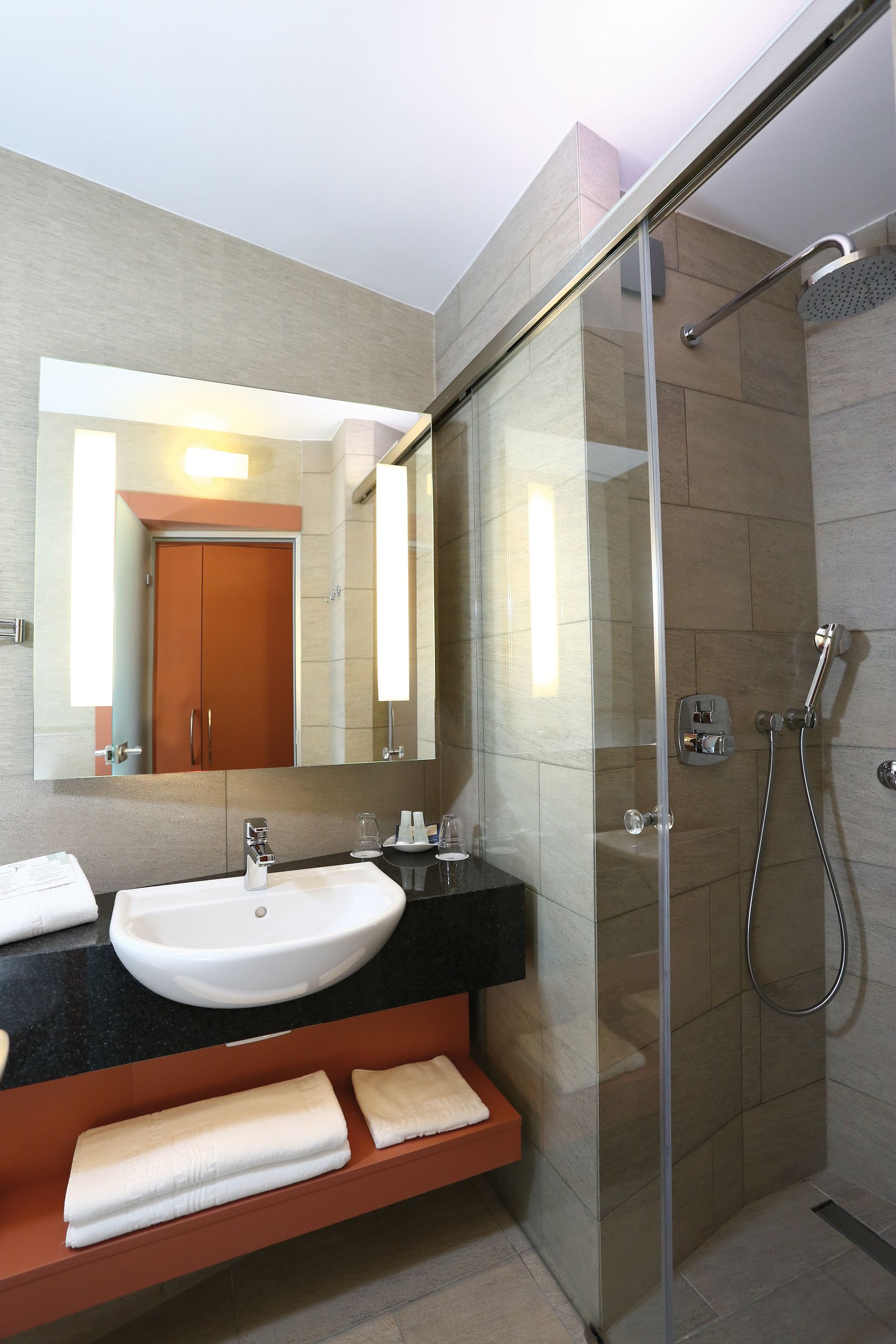 A modern bathroom with a glass-enclosed shower, a white sink, and a large mirror.