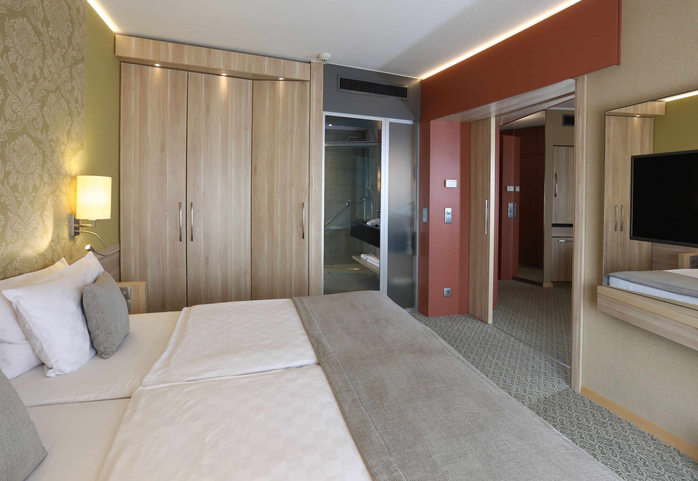 A hotel room with a large bed, a TV, a wardrobe, and a bathroom visible through an open door.