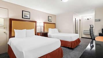 A hotel room with two beds, a desk, a chair, and a door.