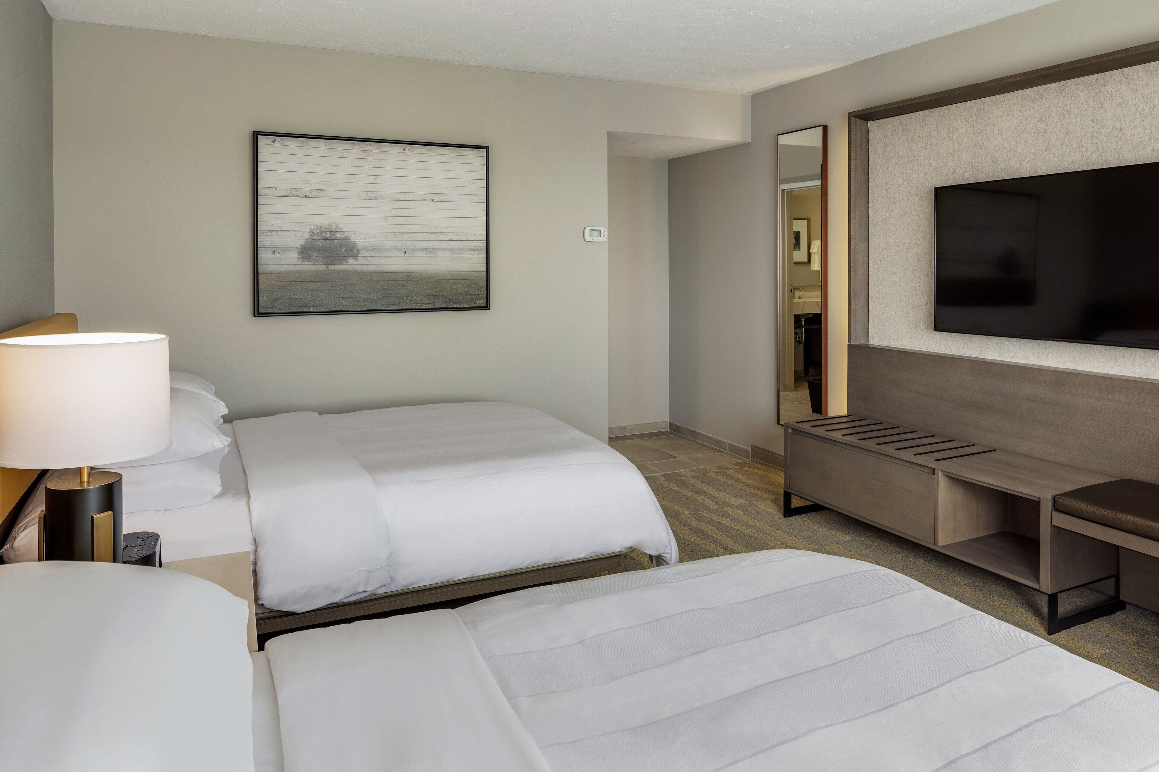 Une chambre d’hôtel avec deux lits, une télévision, un bureau et une grande fenêtre.