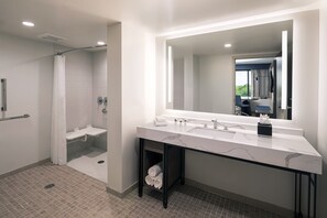 Ein modernes Badezimmer mit einem großen Spiegel, einer Dusche und einem Waschtisch mit Spüle und Handtuchhalter.