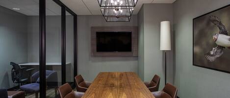 A conference room with a wooden table, leather chairs, a flat-screen TV, a large painting, and a floor lamp.