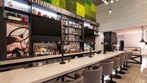Zona de bar moderna amb un comptador llarg, diversos taburets i una varietat de botelles i vasos.