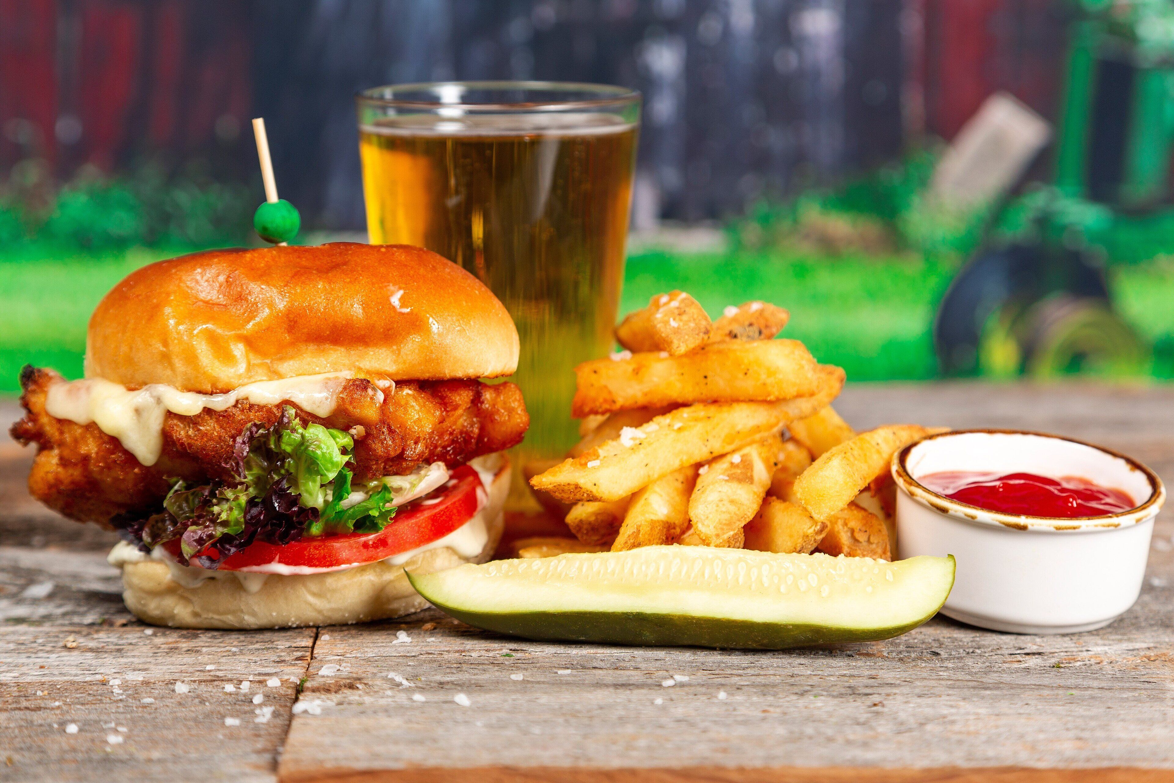 Un repas composé d’un sandwich au poisson, de frites, d’un cornichon, d’un verre de bière et d’un petit bol de ketchup.