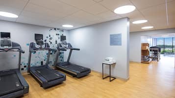 A fitness center with treadmills, a wall-mounted screen, and a small table with towels.