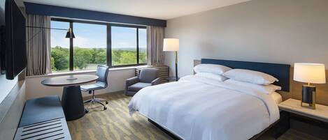 A hotel room with a large bed, a desk, a chair, a small table, and a TV.