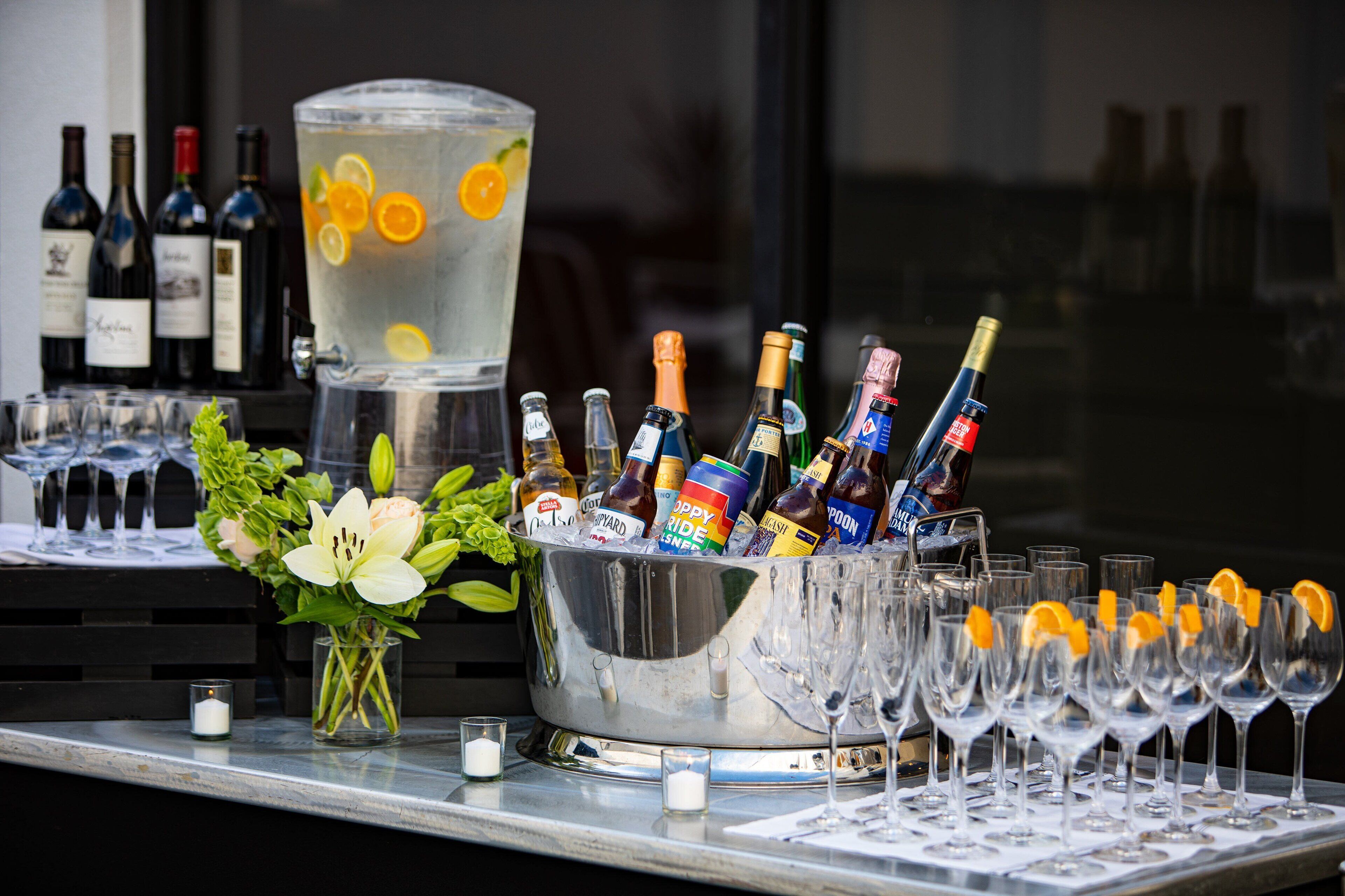 A bar area with a large ice bucket containing various bottles and glasses, a floral arrangement, and a backdrop of wine bottles.