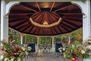 Ein Pavillon mit Holzboden und einer zentralen Chandeliebre, umgeben von Tischen und Stühlen und mit Blumen geschmückt.
