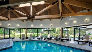Una piscina interior amb sostre de fusta, seients de relax i grans finestres que donen vista a l'exterior.