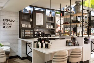 Un área de bar moderna con mostrador blanco, estantes con botellas y una pizarra de menú.