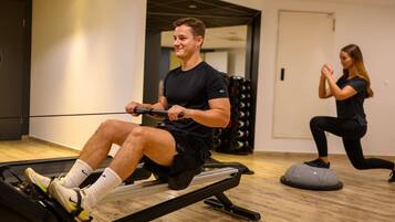 A man using a rowing machine and a woman doing squats in a gym with wooden flooring and a modern design.