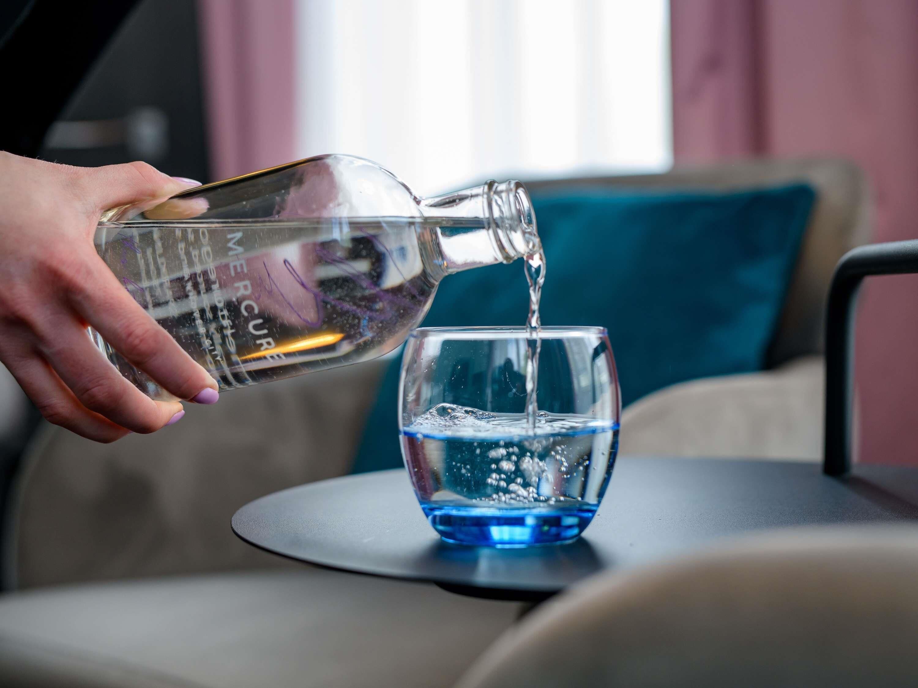 Una mano versa dell'acqua da una bottiglia in un bicchiere su un tavolo.
