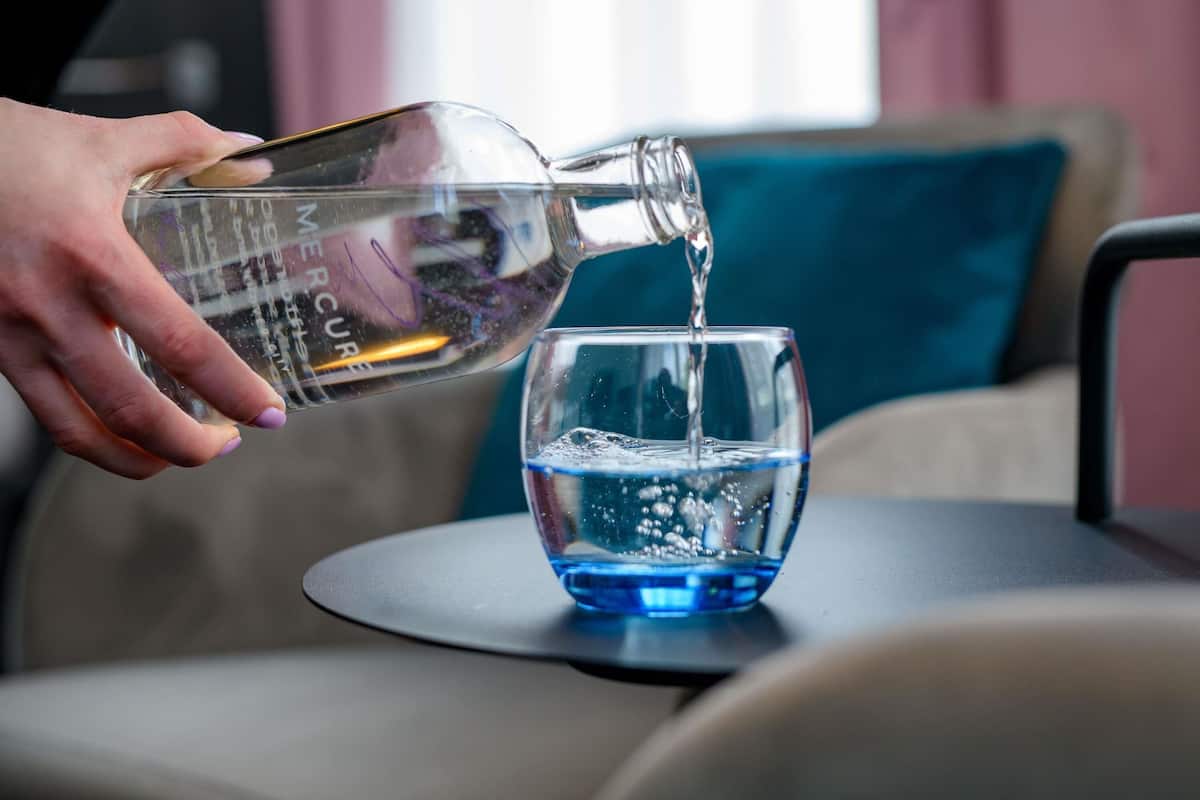 A hand pouring water from a bottle into a glass on a table.