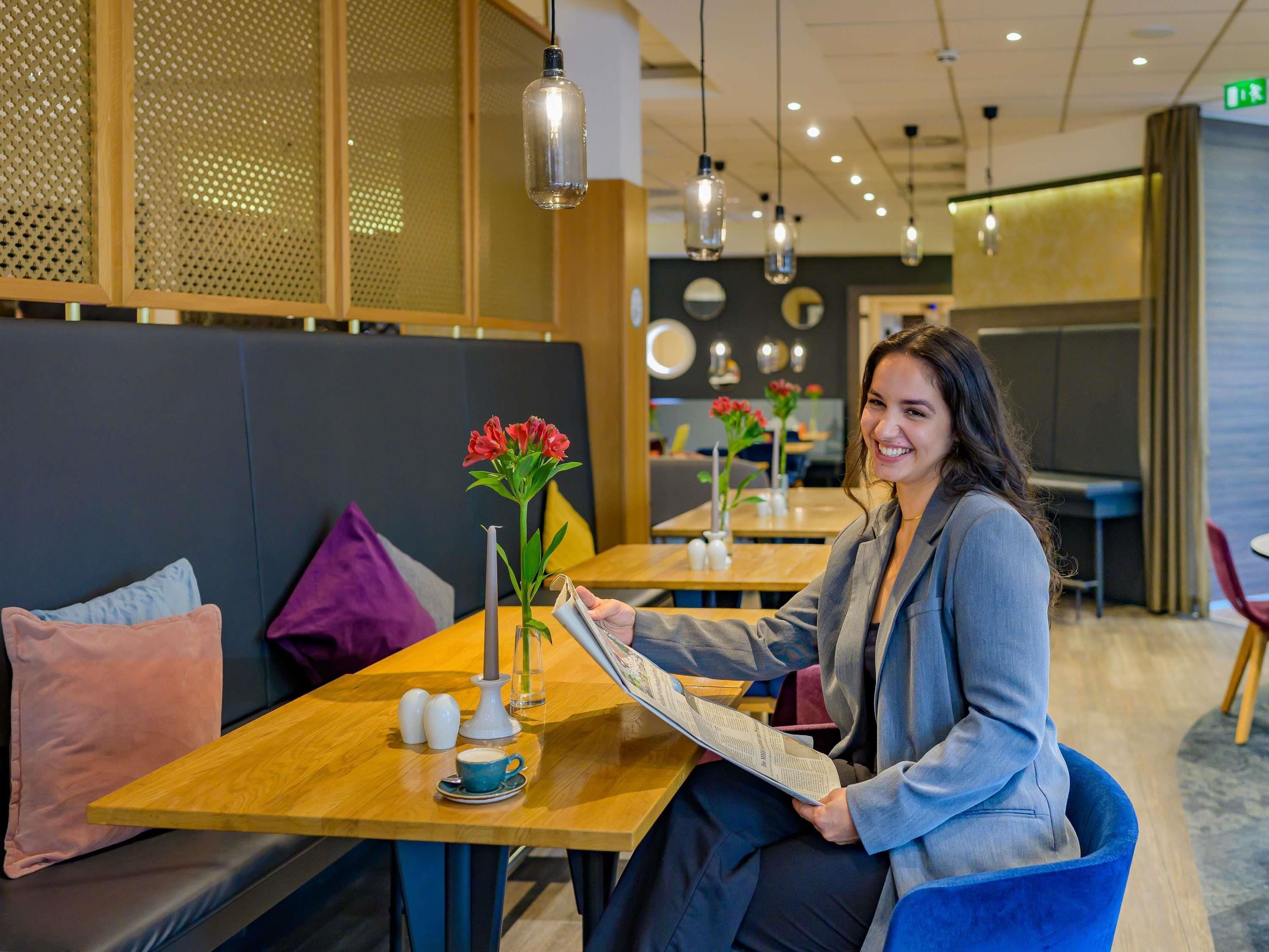 A person seated at a wooden table with a menu, a vase with flowers, and a cup.
