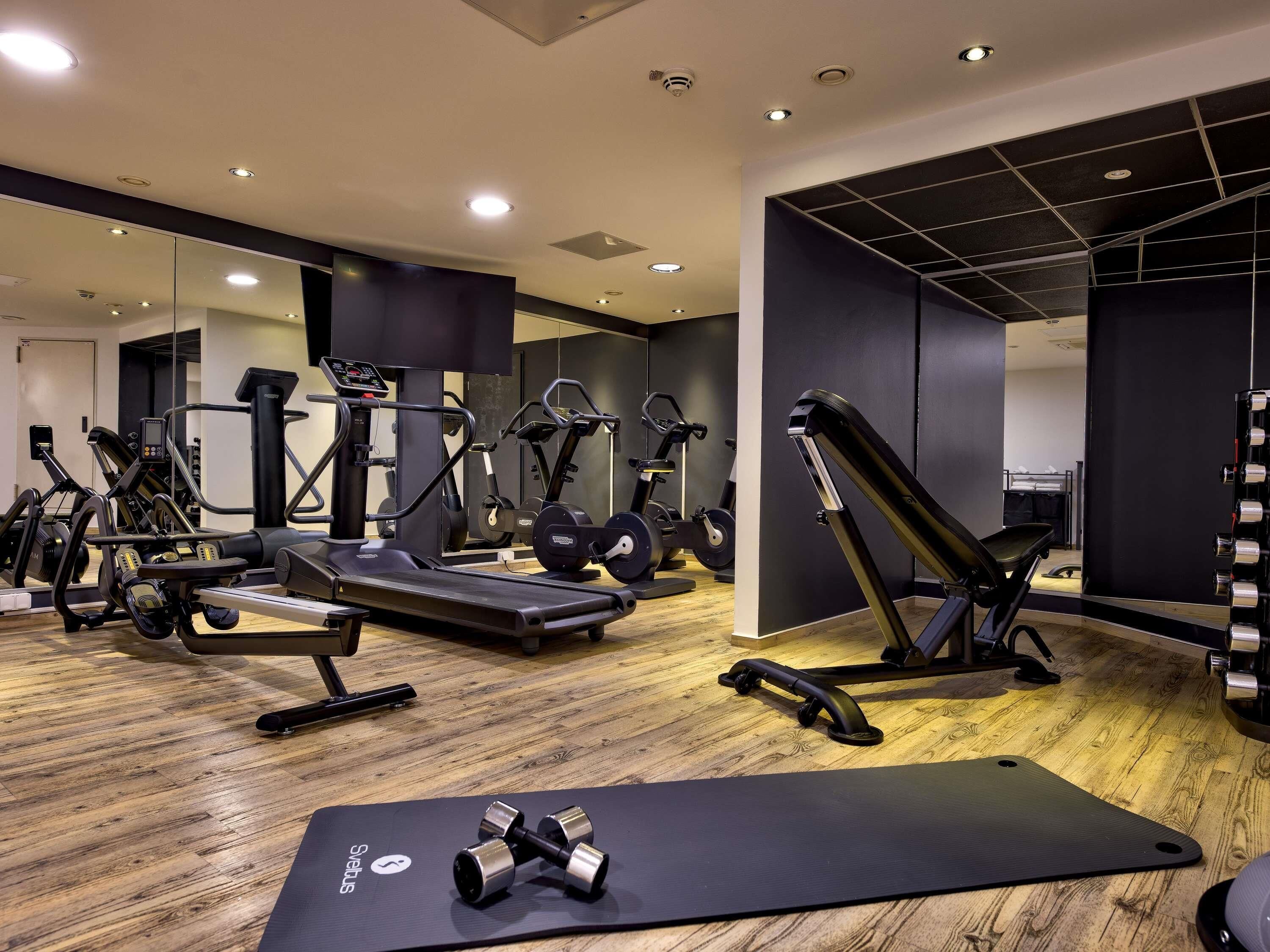 A gym with various exercise equipment, a mirrored wall, and a wooden floor.