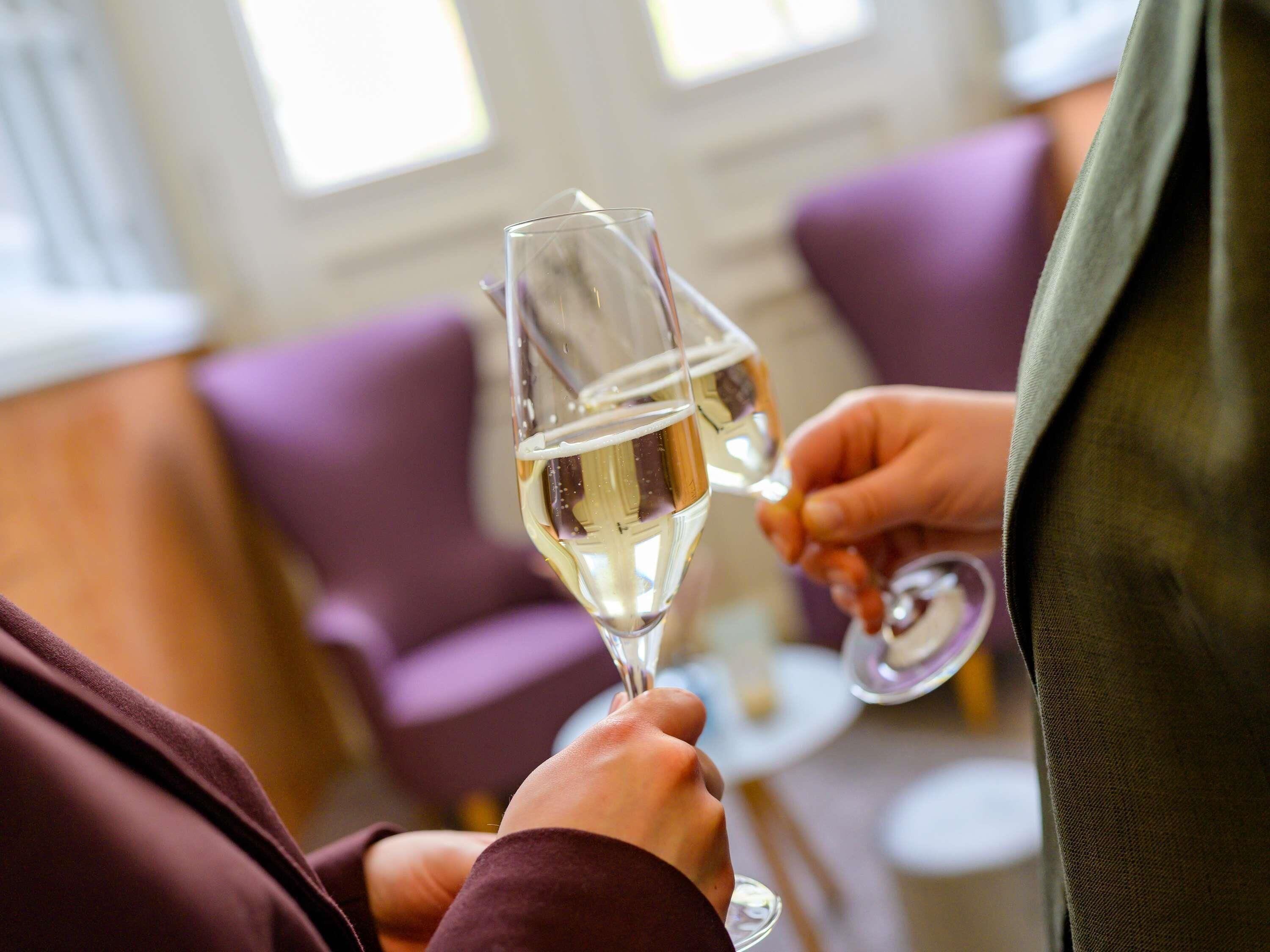 Two people holding wine glasses in a room with purple upholstered chairs and a round table.