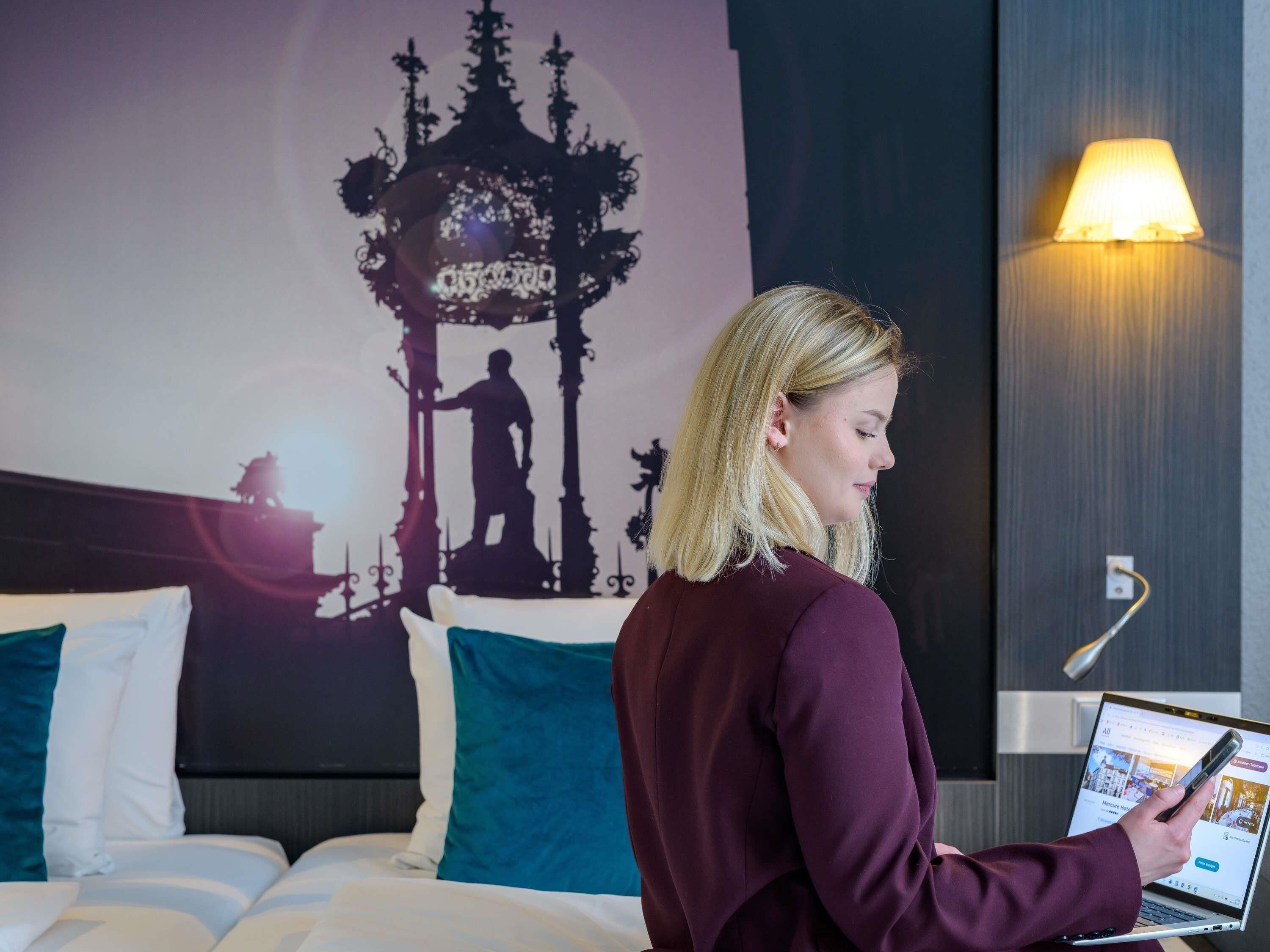 A hotel room with a bed, a laptop, and a wall with a silhouette of a person.