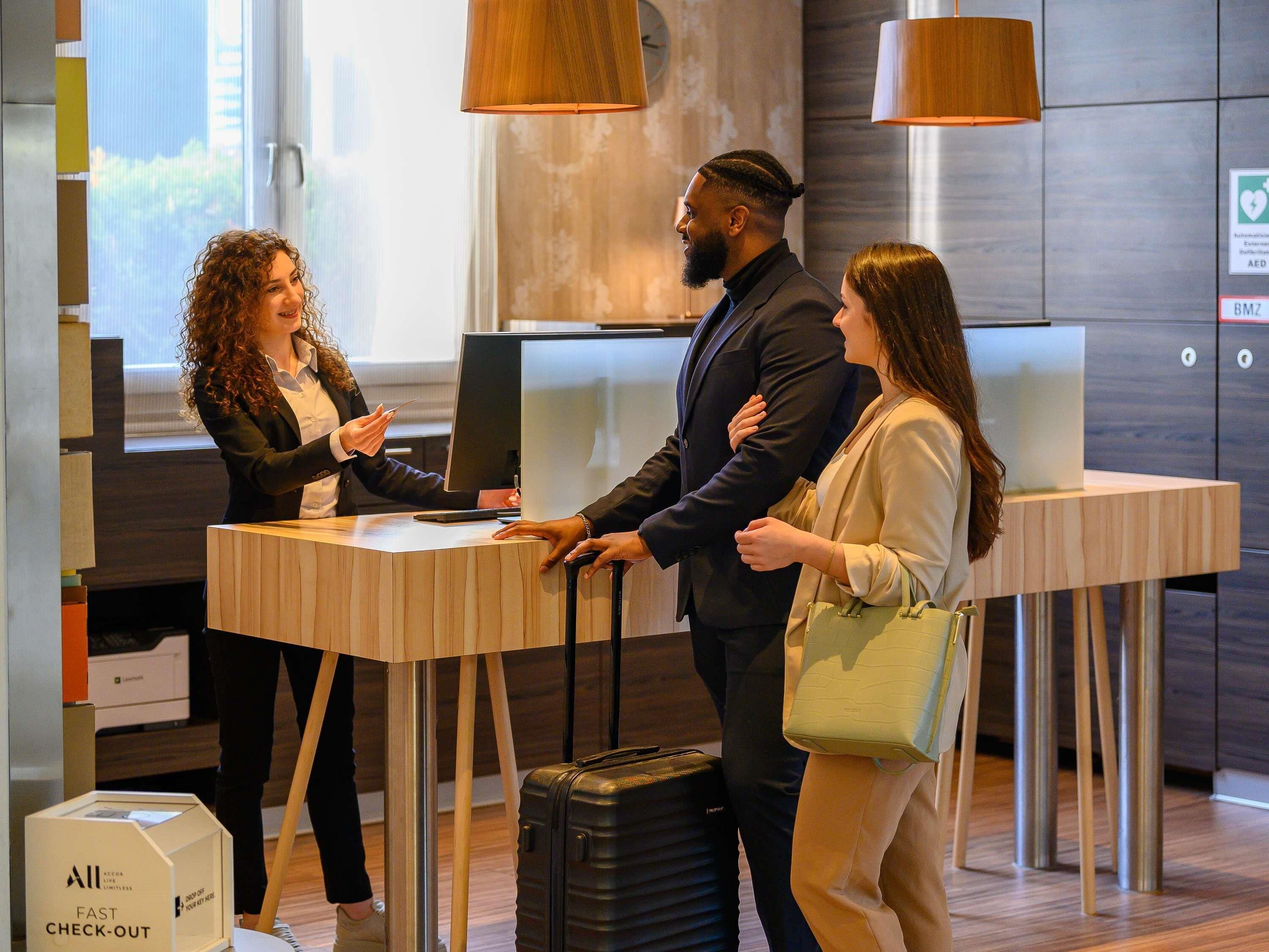A hotel reception desk with a check-out counter, a digital screen, and a sign indicating an AED is available.