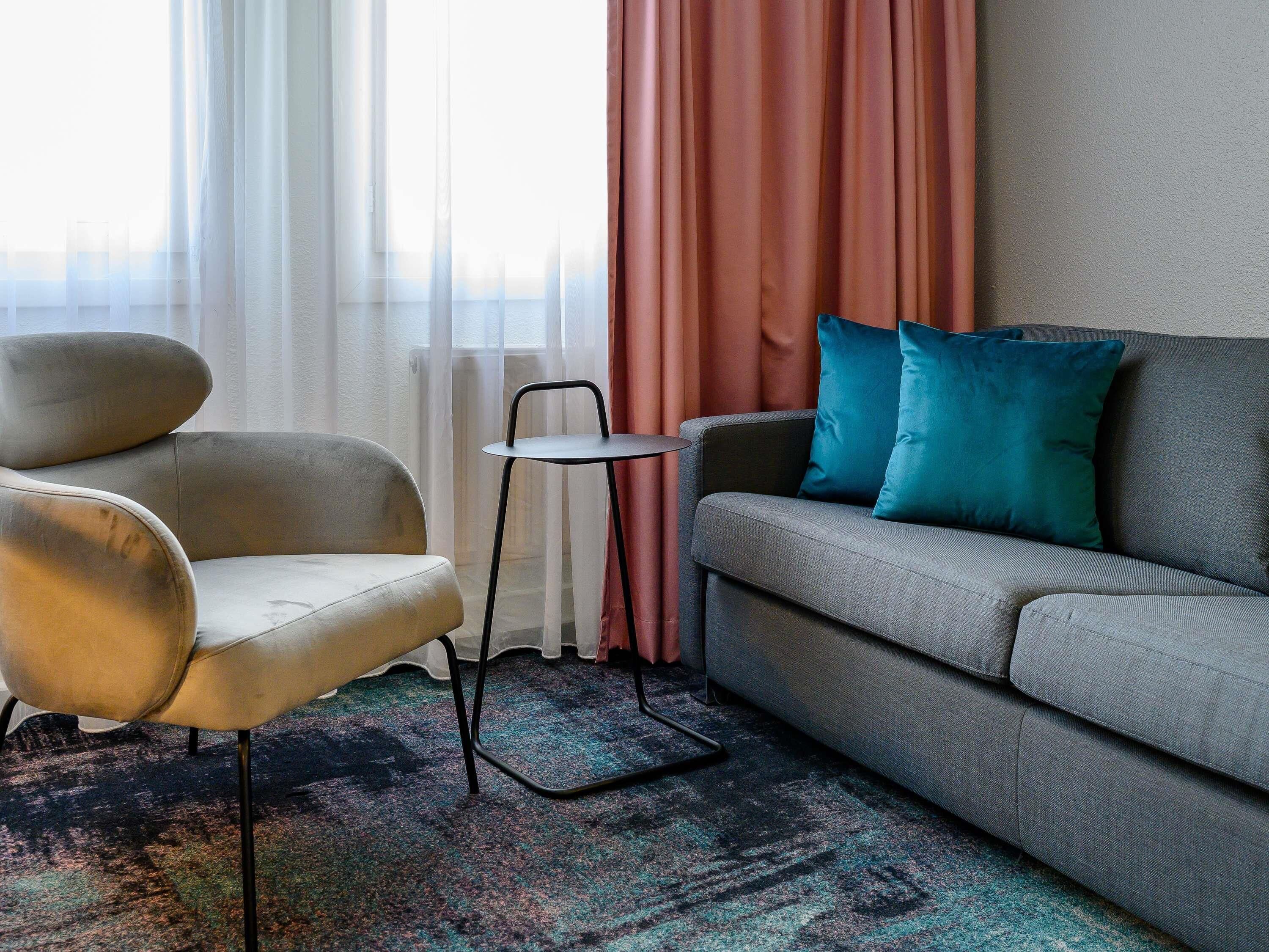 Ein modernes Wohnzimmer mit einem grauen Sofa, einem beigefarbenen Sessel und einem kleinen Beistelltisch.