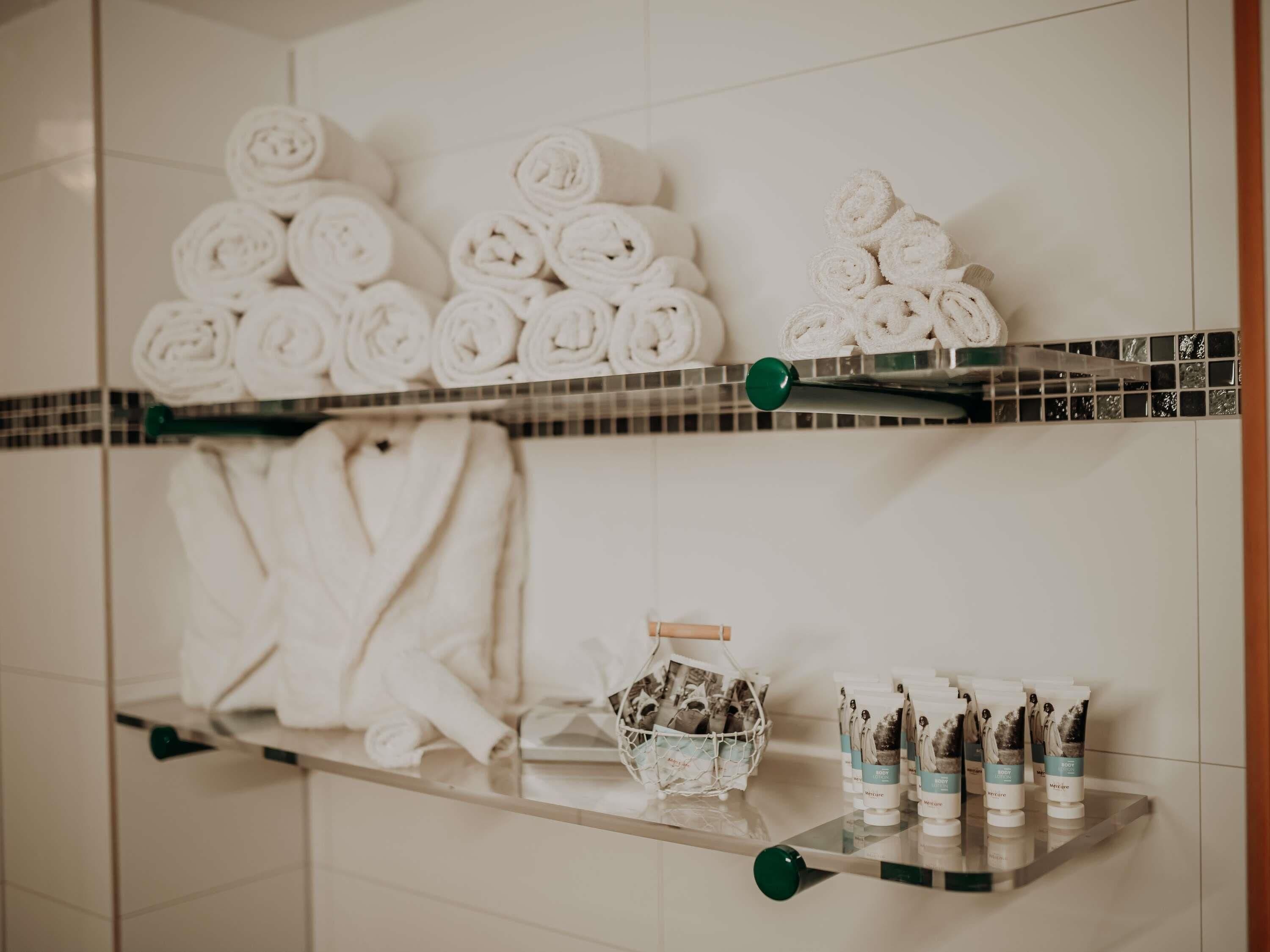Un baño con repisas que contienen toallas enrolladas y artículos de aseo.