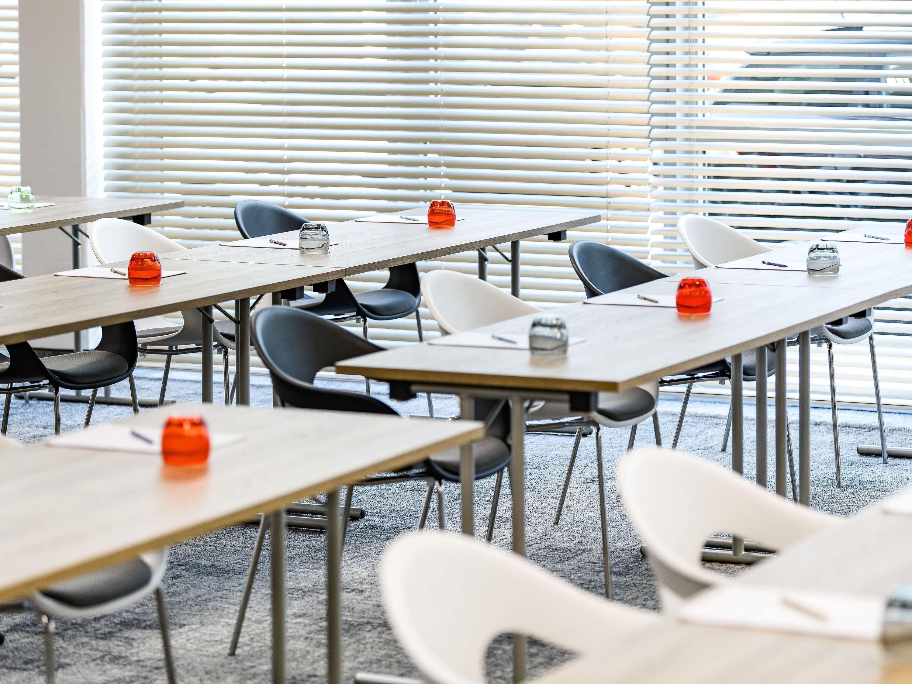 A conference room with multiple tables, chairs, and a window with blinds.