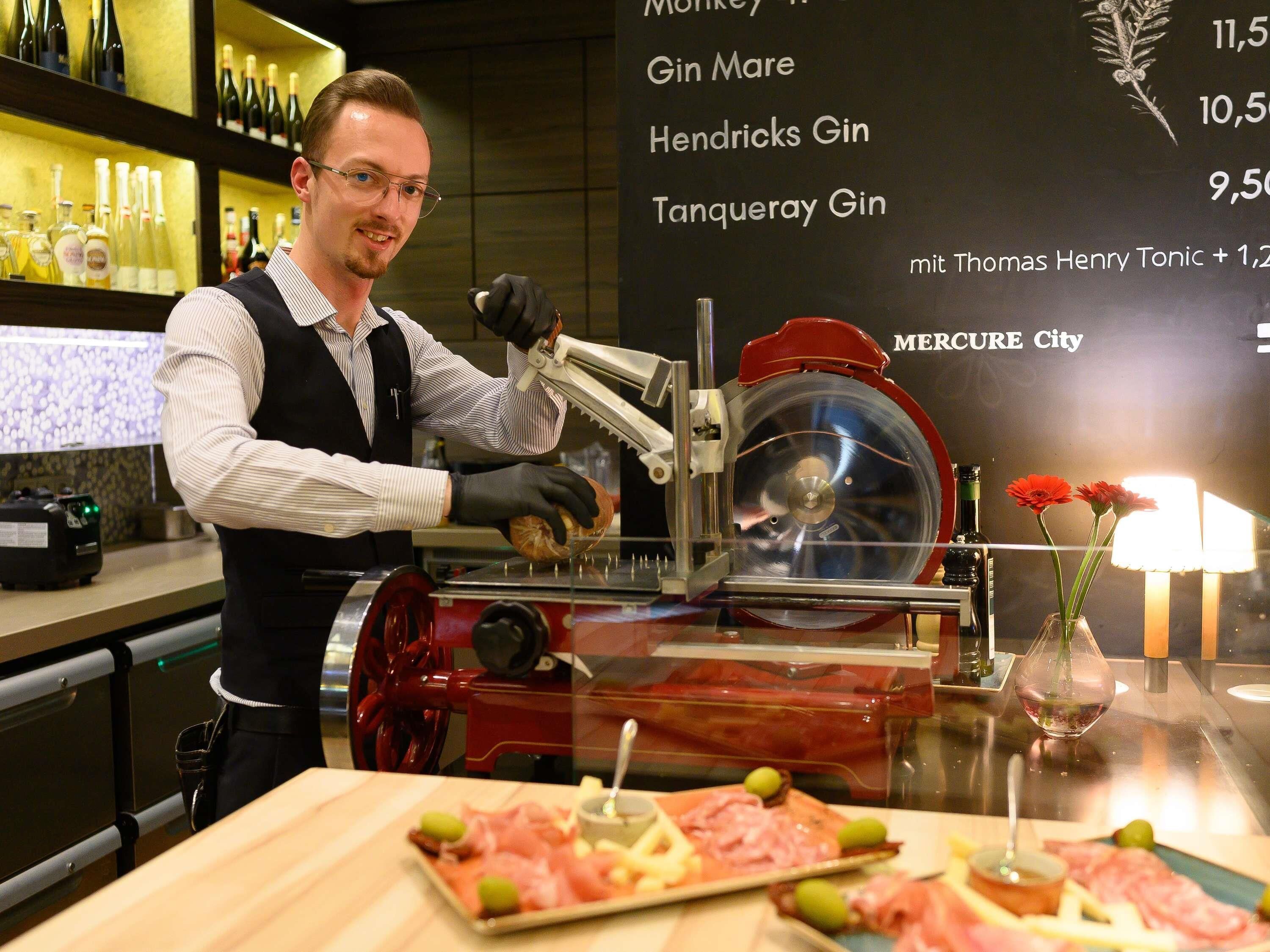 Een persoon bedient een vleessnijmachine achter een bar, met een menukaart op de achtergrond.