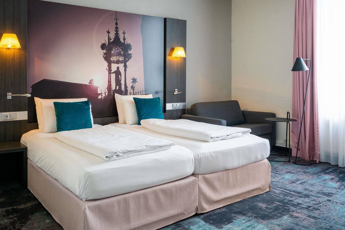 Een hotelkamer met twee bedden, een bank, een kleine tafel en een wandlamp.