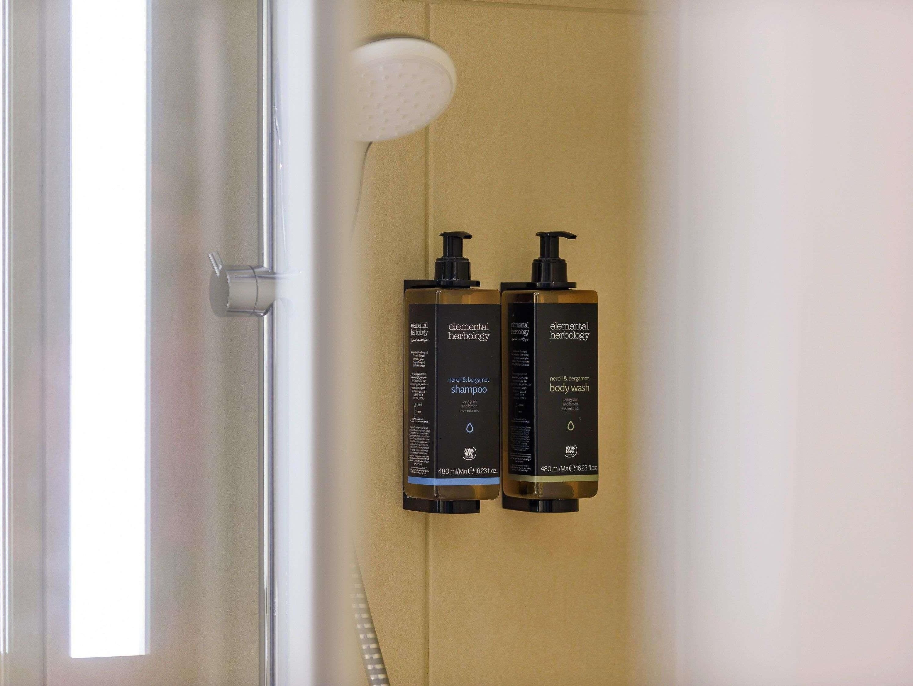 A bathroom with two bottles of elemental herbology shampoo and body wash, a showerhead, and a door.