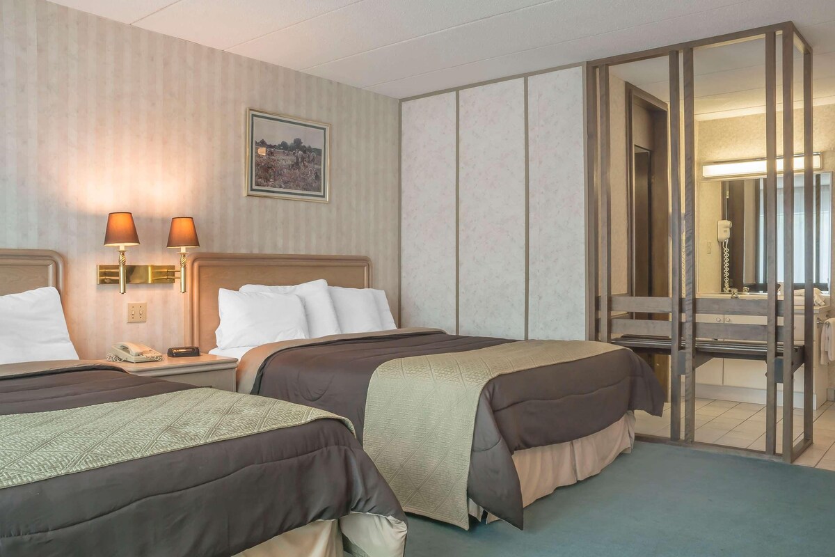 A hotel room with two beds, a bedside table with a lamp, a telephone, and a framed picture on the wall.