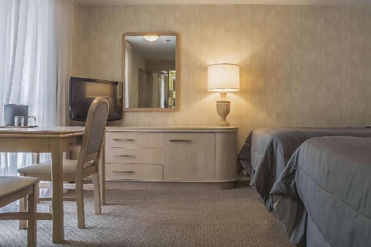 A hotel room with a bed, a desk with a chair, a television, a lamp, and a dresser.