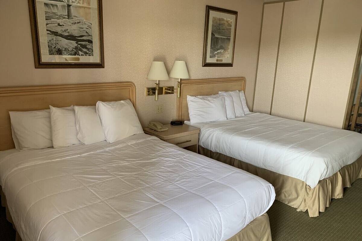 A hotel room with two beds, a nightstand, a lamp, and framed pictures on the wall.