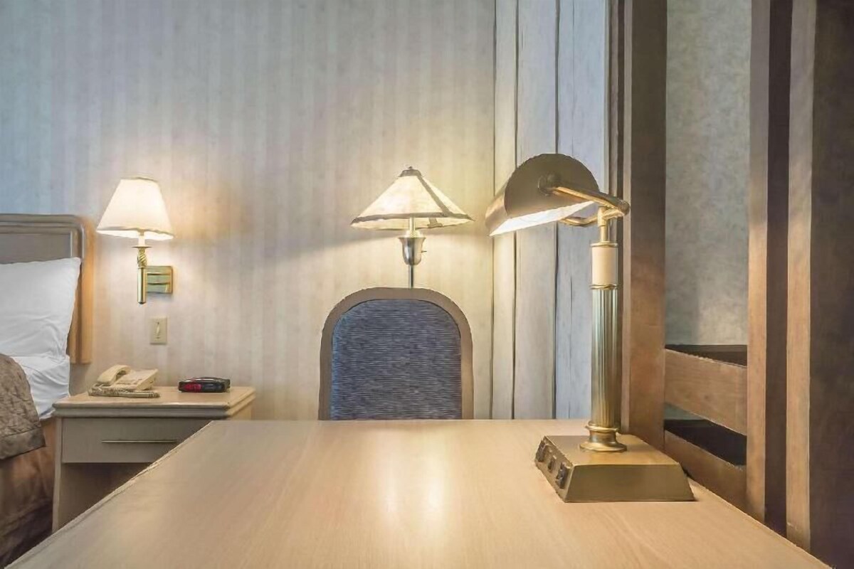 A hotel room with a bed, a nightstand with a lamp, a table, and a chair.