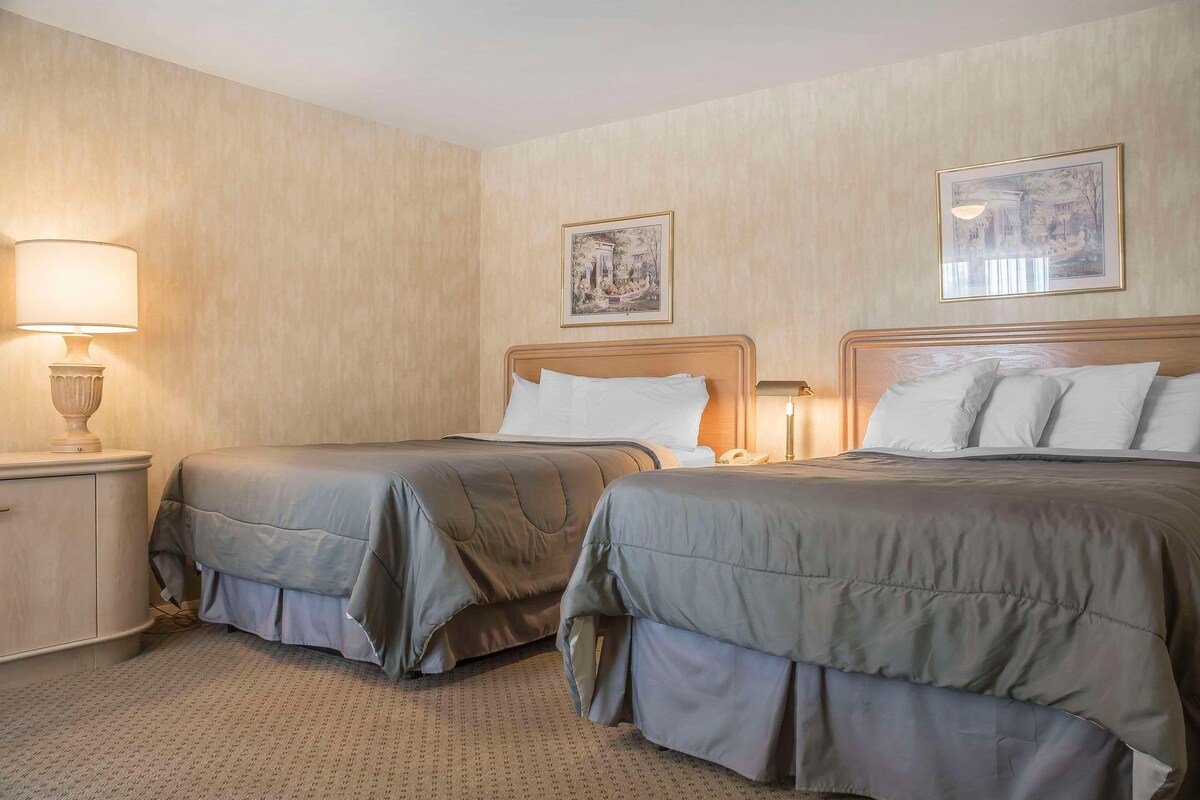 A hotel room with two beds, a nightstand, a lamp, and two framed pictures on the wall.