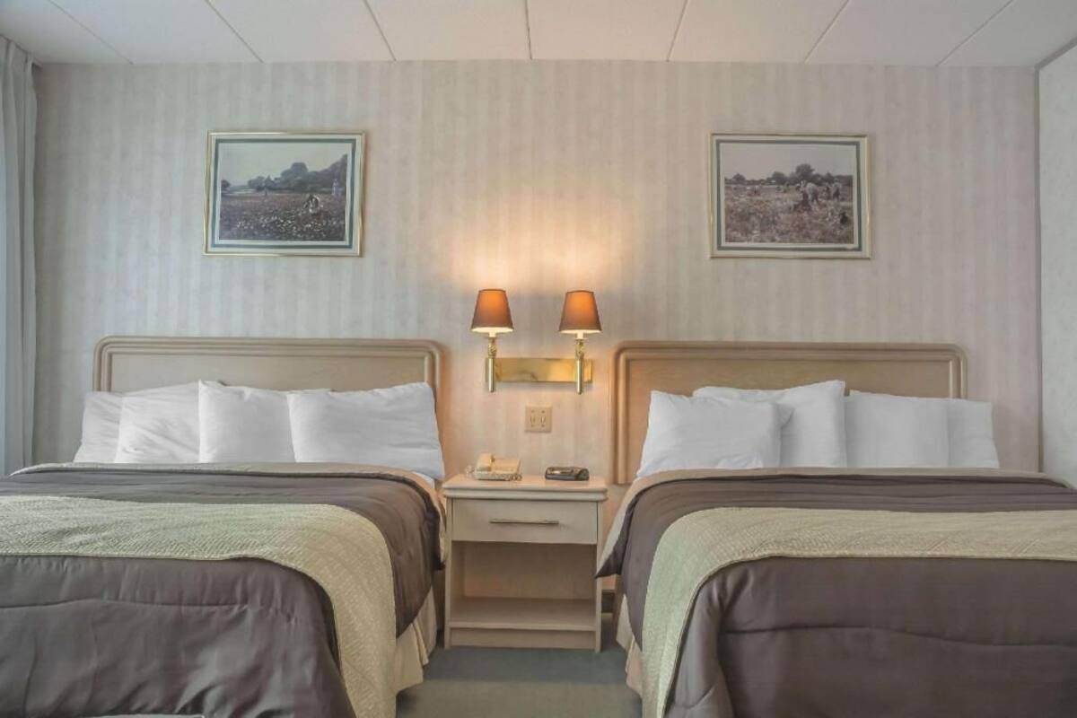 A hotel room with two beds, a nightstand with lamps, and two framed pictures on the wall.