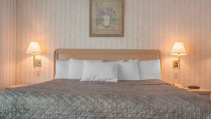 A hotel room with a large bed, two bedside lamps, a framed picture on the wall, and a nightstand with a phone and a digital clock. - Rodeway Inn Fallsview (Niagara Falls)