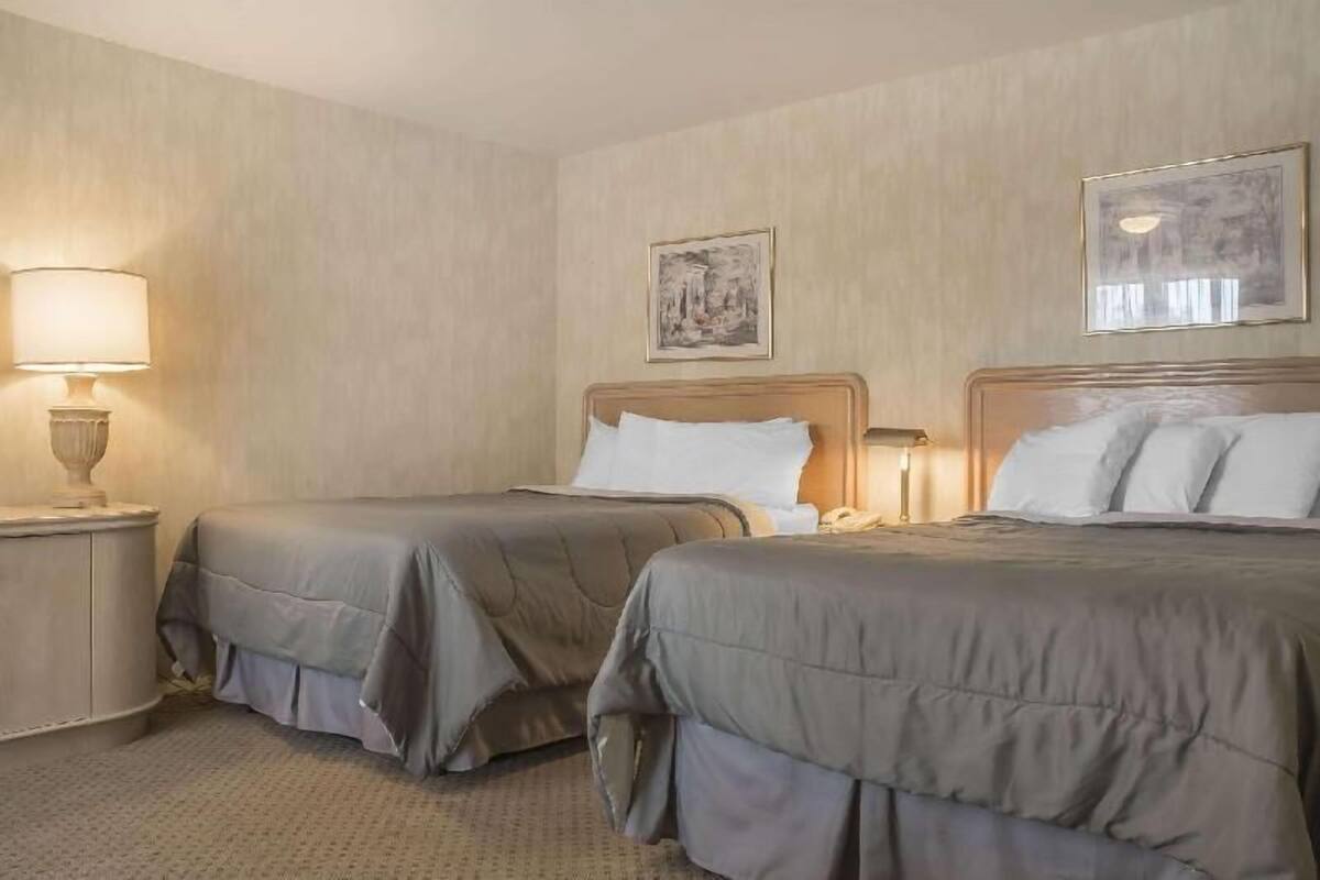 A hotel room with two beds, a nightstand with a lamp, and a framed picture on the wall.