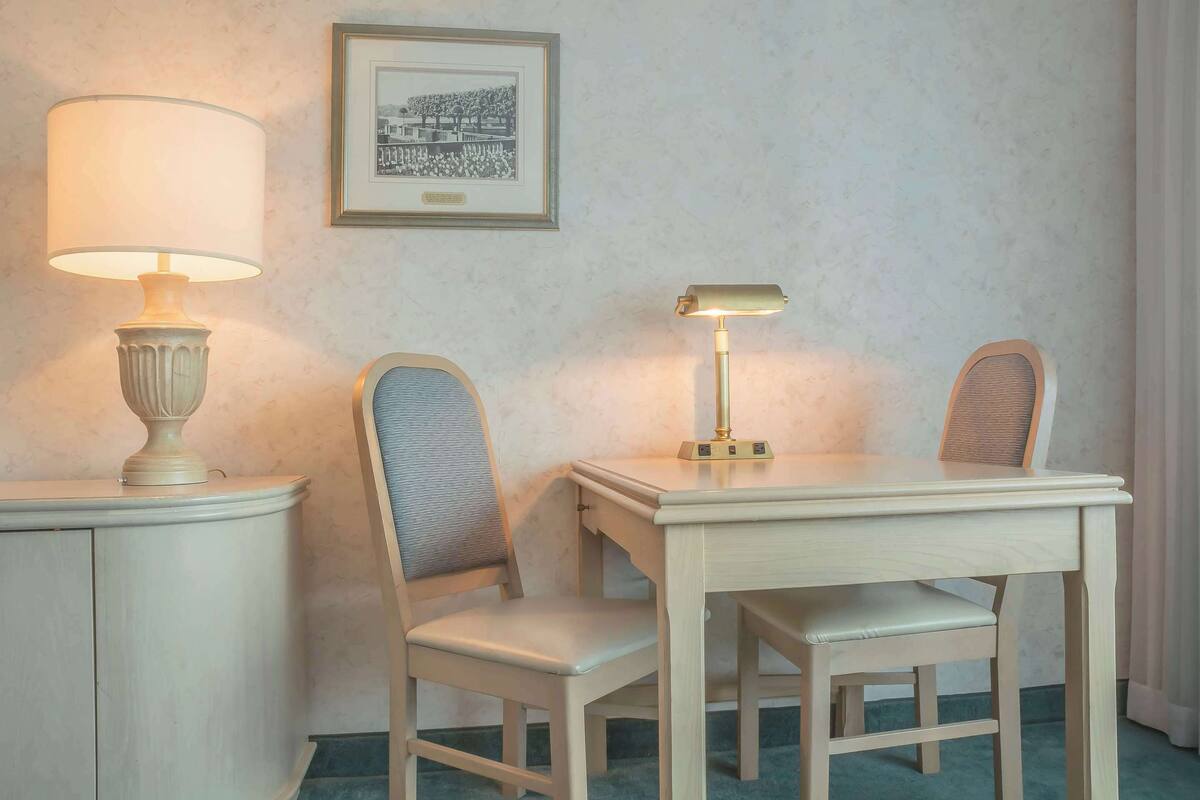 A room with a desk, two chairs, a lamp, and a framed picture on the wall.