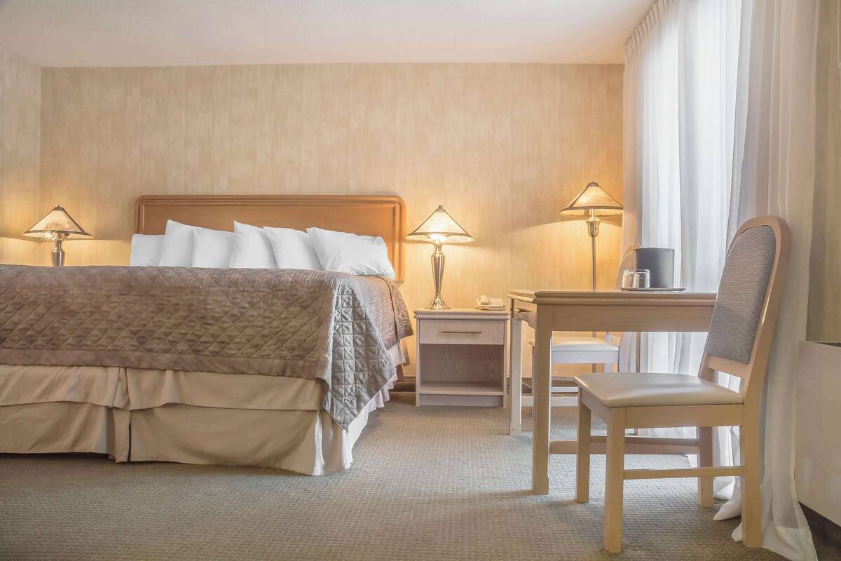 A hotel room with a bed, bedside tables, a desk, a chair, and lamps.
