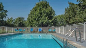 A swimming pool with clear blue water, surrounded by a metal fence and blue lounge chairs. - Rodeway Inn Fallsview (Niagara Falls)