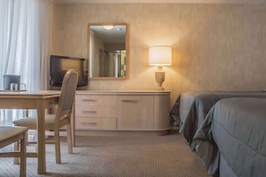 Et hotelværelse med skrivebord, stol, fjernsyn, spejl, natbord med lampe og seng.